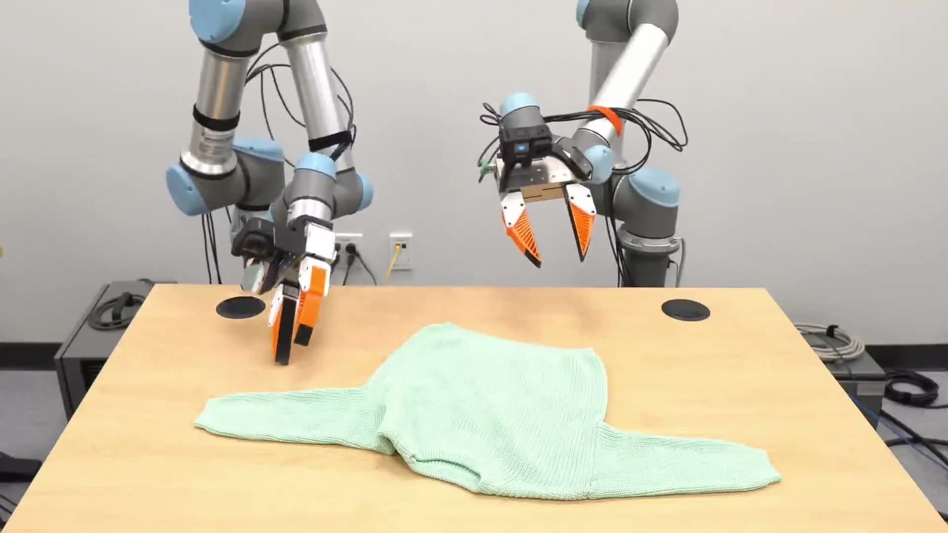 Two robot arms with UMI grippers folding a garment on a table
